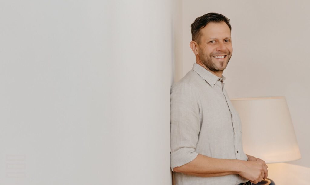 Familien- und Wirtschaftsmediator Sören Peter steht freundlich lachend an einer Wand. Im Hintergrund eine Stehleuchte.